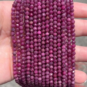 May include: A collection of multiple strands of small, round, faceted ruby beads in a deep magenta-pink colour. The beads are uniform in size and shape, featuring a reflective, textured surface that catches the light across the entire arrangement.