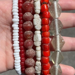 May include: A collection of beaded bracelets in various styles and colors. The bracelets feature white, red, and clear beads, with some having unique textures and shapes. The beads are strung together, creating a visually appealing and diverse set of accessories.