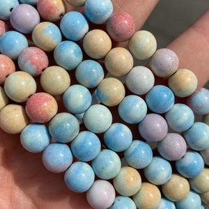 May include: A strand of round, ceramic beads in shades of blue, pink, and yellow. The beads have a speckled, marbled appearance.