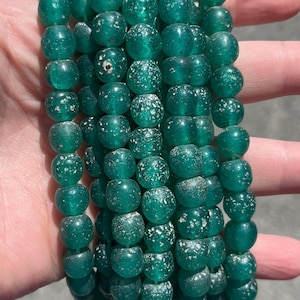 May include: Strands of teal glass beads. The beads are round with a flattened shape and a frosted, speckled appearance. The beads are strung together, creating a necklace or bracelet.