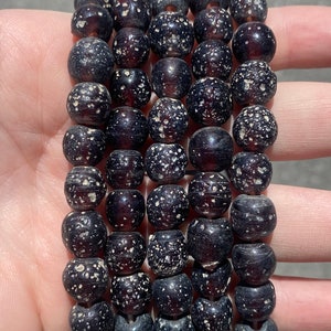May include: A stack of five bracelets made of dark brown wooden beads with white speckles.