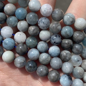 May include: A strand of light blue and grey gemstone beads. The beads are round and have a smooth, polished finish.