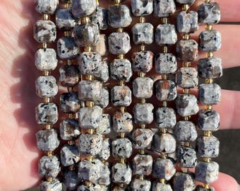 May include: A necklace or bracelet featuring square-cut beads in shades of grey and brown, interspersed with gold-coloured spacers. The beads display a speckled pattern.