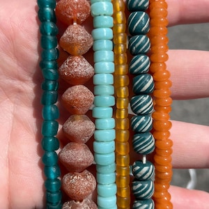 May include: A collection of colorful beaded bracelets. The bracelets feature various bead shapes and colors, including teal, orange, light blue, and amber. Some beads have white stripes. The bracelets are strung together, showcasing a variety of textures and designs.