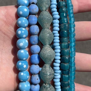 May include: A collection of beaded bracelets in shades of blue. The bracelets feature various bead styles, including polka-dotted, round, and faceted beads. The color palette ranges from light to deep blue, creating a visually appealing contrast.