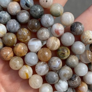 May include: A strand of round agate beads in various shades of brown, grey, and white. The beads have a natural, organic look with swirling patterns and textures.