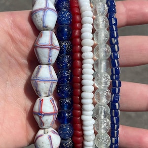May include: A collection of beaded bracelets in various colors. The bracelets include white beads with red and blue accents, dark blue, red, white, clear, and blue beads. The beads are strung together to create a unique accessory.