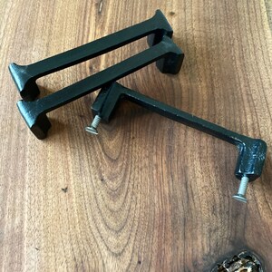 May include: Three black metal cabinet pulls with a simple, modern design. The pulls are shown on a wooden surface.
