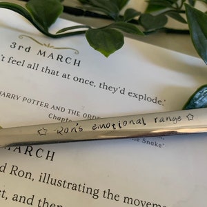 May include: A silver spoon engraved with the words "Ron's emotional range". The spoon is resting on a page from the book "Harry Potter and the Order of the Phoenix", which shows the date "3rd March" printed on the page.