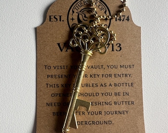May include: A gold-colored key-shaped bottle opener with a decorative design. The key has a chain attached to it and is displayed on a brown card with the text "EST. THE BANK OF 1474 VA 713" and instructions for using the key to visit a vault.