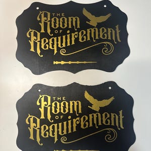 以下が含まれることがあります： 「The Room of Requirement」と金色の文字で書かれた黒い看板が2つ。それぞれの看板には、飛んでいる鳥の金色のシルエットと金色の杖が描かれている。