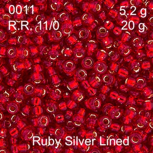 May include: A close-up of a pile of small, red, glass beads with silver lining. The beads are labelled "0011 R.R. 11/0 Ruby Silver Lined" and "5.2g 20g".