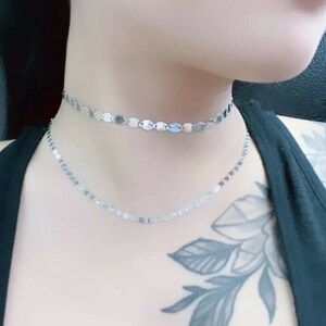 May include: Two silver chain necklaces with small, oval-shaped links. The necklaces are layered, with the shorter one sitting closer to the neck.