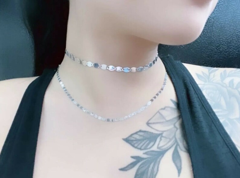 May include: Two silver chain necklaces with small, oval-shaped links. The necklaces are layered, with the shorter one sitting closer to the neck.