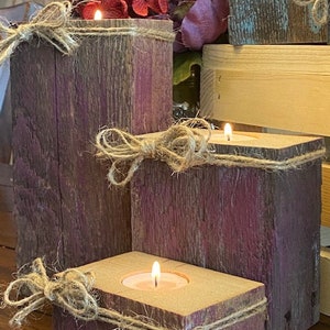 Puede incluir: Tres portavelas de madera r&uacute;stica con una mancha p&uacute;rpura y detalles de cuerda. Cada portavelas tiene una peque&ntilde;a vela de t&eacute;.