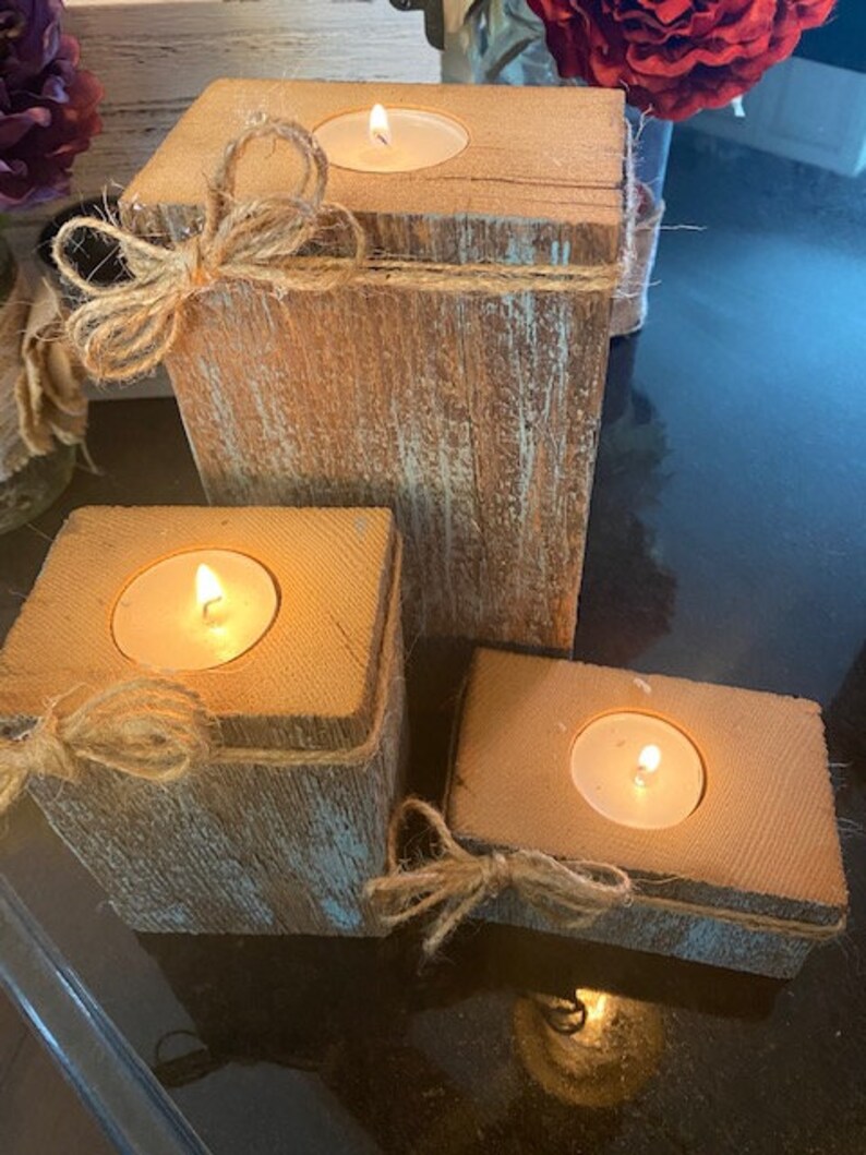 Puede incluir: Tres portavelas de madera r&uacute;stica con detalles de pintura azul verdoso. Cada portavelas tiene una peque&ntilde;a vela de t&eacute; dentro y est&aacute; decorado con lazos de cuerda.