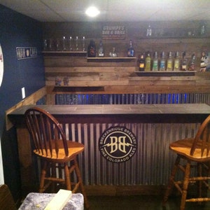 May include: A rustic bar with a wooden countertop and a metal backsplash. The backsplash features a logo for Breckenridge Brewery. Two wooden bar stools are in front of the bar.