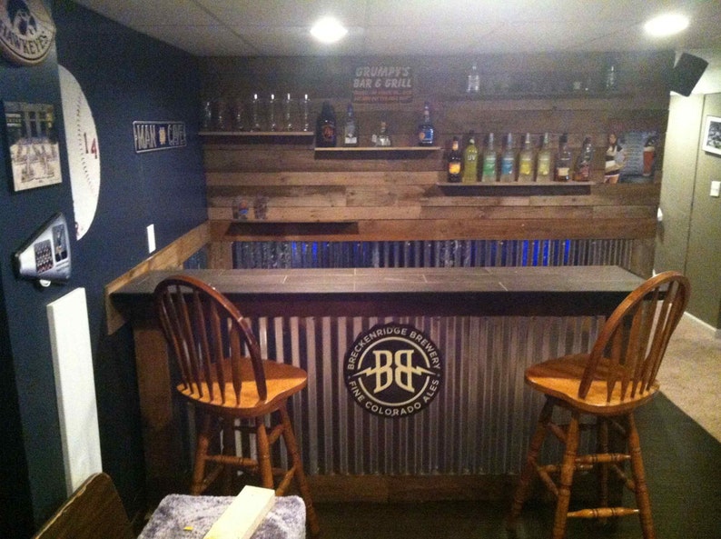 May include: A rustic bar with a wooden countertop and a metal backsplash. The backsplash features a logo for Breckenridge Brewery. Two wooden bar stools are in front of the bar.