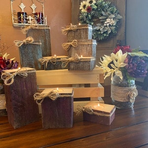 Puede incluir: Un conjunto de candelabros de madera r&uacute;stica con un acabado de madera natural y un aspecto desgastado. Los candelabros est&aacute;n dispuestos sobre una mesa de madera con un jarr&oacute;n de flores en el fondo.