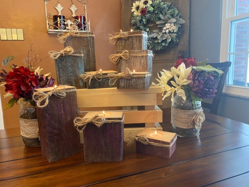 Puede incluir: Un conjunto de candelabros de madera r&uacute;stica con un acabado de madera natural y un aspecto desgastado. Los candelabros est&aacute;n dispuestos sobre una mesa de madera con un jarr&oacute;n de flores en el fondo.