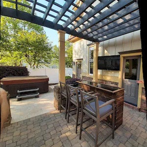 May include: Outdoor patio with a wooden bar, two bar stools, a hot tub, and a pergola with a large TV mounted on the wall.