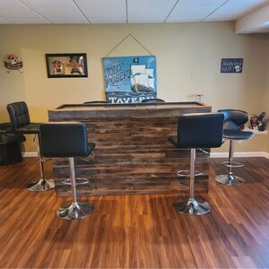 May include: A rustic wooden bar with a distressed finish, featuring a built-in shelf and four black bar stools with chrome bases. The bar is decorated with a nautical-themed sign that reads "The Jolly Roger Tavern".