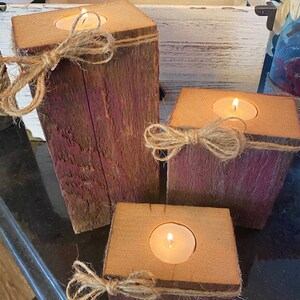 Puede incluir: Tres portavelas de madera r&uacute;stica con un acabado de pintura p&uacute;rpura desgastada. Cada portavelas tiene una peque&ntilde;a abertura redonda para una vela de t&eacute; y est&aacute; decorado con un lazo de cuerda natural.