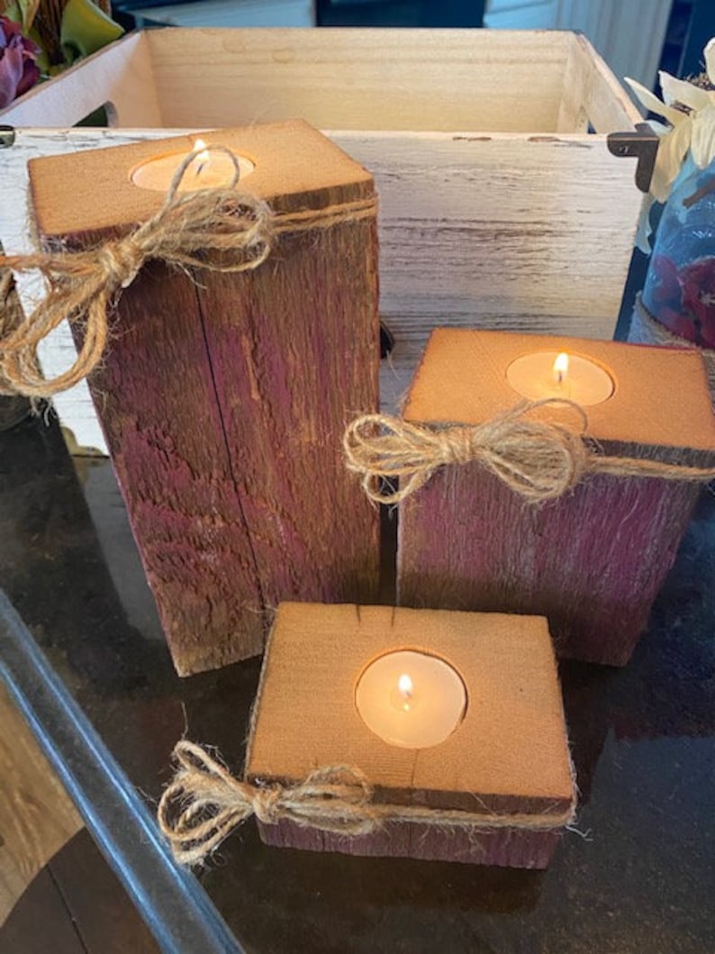 Puede incluir: Tres portavelas de madera r&uacute;stica con un acabado de pintura p&uacute;rpura desgastada. Cada portavelas tiene una peque&ntilde;a abertura redonda para una vela de t&eacute; y est&aacute; decorado con un lazo de cuerda natural.
