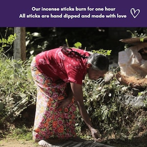 May include: A woman in a red and floral patterned dress is hand-making incense sticks outdoors. The sticks are laid out on a woven mat.