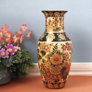 May include: A decorative ceramic vase featuring a black and cream background with intricate floral patterns in red, gold, and black. The vase has a flared rim and a tapered neck, adorned with detailed botanical motifs and geometric shapes throughout.