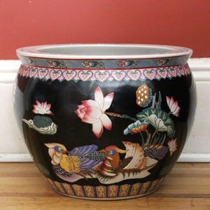 May include: A round ceramic fishbowl featuring a black background with hand-painted illustrations of colourful mandarin ducks, pink lotus flowers, and green lily pads. The rim and base are decorated with intricate pink, blue, and gold patterns.