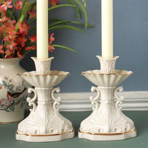 Peut inclure: Une paire de bougeoirs en céramique blanc cassé avec des détails en relief en forme de feuilles, un plateau festonné avec un bord doré fin et des poignées latérales en volutes, chacun supportant une bougie effilée longue et fine.