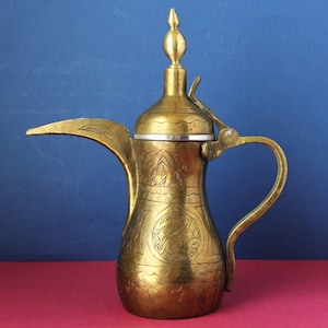 Könnte beinhalten: Eine Vintage-Kaffeekanne aus Messing mit langem Ausguss und gebogenem Griff. Die Kanne weist aufwendige geätzte Designs und einen spitzen Deckel auf. Das Metall hat einen warmen, goldenen Farbton, und die Kanne wird wahrscheinlich zum Servieren von Kaffee oder Tee verwendet.