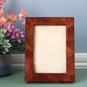 May include: A rectangular wooden picture frame with a rich, dark brown finish. The frame has a visible wood grain pattern and a cream-colored interior. The frame is standing upright on a surface, ready to display a photograph or artwork.