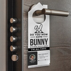 Op de afbeelding: Een witte deurhanger met een konijnenillustratie en de tekst "Do you now some bunny with real estate needs? I'm all ears."  De deurhanger bevat ook een visitekaartje met de naam Joanna Smith, makelaar en de contactgegevens van Your Town Realty.