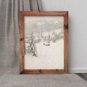 May include: A framed landscape painting depicts a snowy mountain scene with evergreen trees and a figure. The artwork is encased in a rustic, rectangular wooden frame. The overall color palette is muted, with shades of white, gray, and brown.