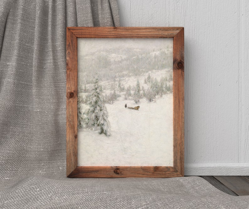 May include: A framed landscape painting depicts a snowy mountain scene with evergreen trees and a figure. The artwork is encased in a rustic, rectangular wooden frame. The overall color palette is muted, with shades of white, gray, and brown.