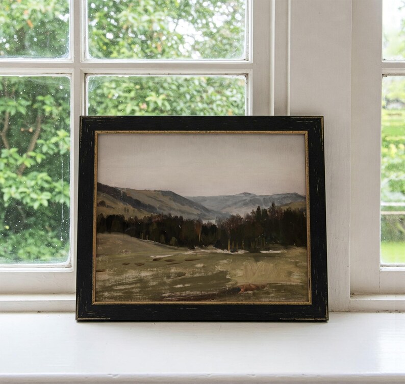 May include: A framed landscape painting depicting a valley with rolling hills and a forest in the distance. The painting is in a black frame with a gold trim.