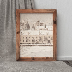 May include: A framed watercolor painting of a snowy cityscape with brown buildings and trees. The painting is in a rustic wooden frame.