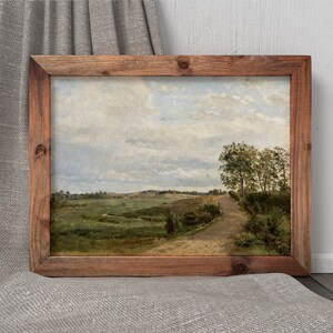 Pu&ograve; includere: Un dipinto incorniciato di un paesaggio rurale con una strada sterrata che attraversa un campo. Il cielo &egrave; nuvoloso e gli alberi sono verdi.