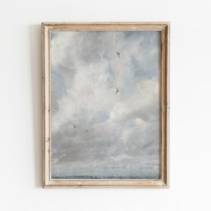 May include: A framed painting of a cloudy sky with a few birds flying in formation. The sky is a light blue with white clouds and the water is a dark blue.