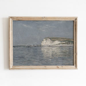 Może przedstawiać: Namalowany obraz w ramie przedstawiający krajobraz morski z białą klifem w oddali. Niebo jest jasnoniebieskie, a woda jest spokojna i odbijająca błękit. Obraz jest w prostej drewnianej ramie.