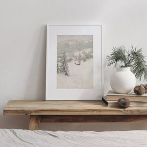 May include: A framed print of a snowy mountain landscape rests on a wooden bench. A white vase with greenery and decorative paper ornaments sit nearby. The scene evokes a sense of winter and nature.
