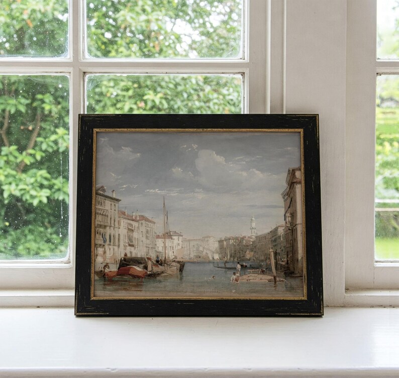 K&ouml;nnte beinhalten: Ein gerahmtes Aquarellbild, das eine Kanalszene in Venedig, Italien, darstellt. Das Bild zeigt einen schmalen Kanal mit Geb&auml;uden an beiden Seiten. Es befinden sich mehrere Boote im Wasser, darunter eine Gondel. Der Himmel ist hellblau mit einigen Wolken.