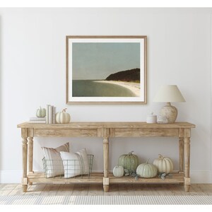 May include: A wooden console table with a framed seascape print above it. The table has two shelves and is decorated with pumpkins and a lamp.