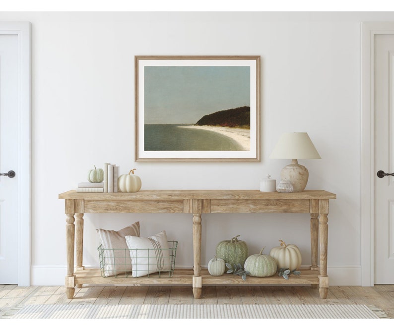 May include: A wooden console table with a framed seascape print above it. The table has two shelves and is decorated with pumpkins and a lamp.