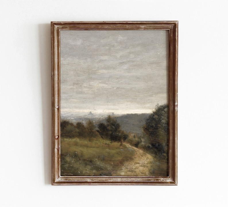 May include: A framed painting of a landscape with a winding dirt path leading through a field of green grass and trees. The sky is a muted gray with a few clouds.