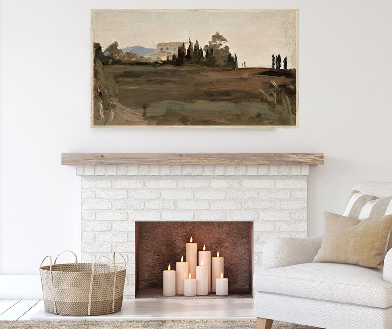 May include: A white brick fireplace with a wooden mantel and a brown hearth. There are several white pillar candles lit inside the fireplace. A white armchair with a beige throw pillow is in the foreground. A wicker basket is on the floor in front of the fireplace.