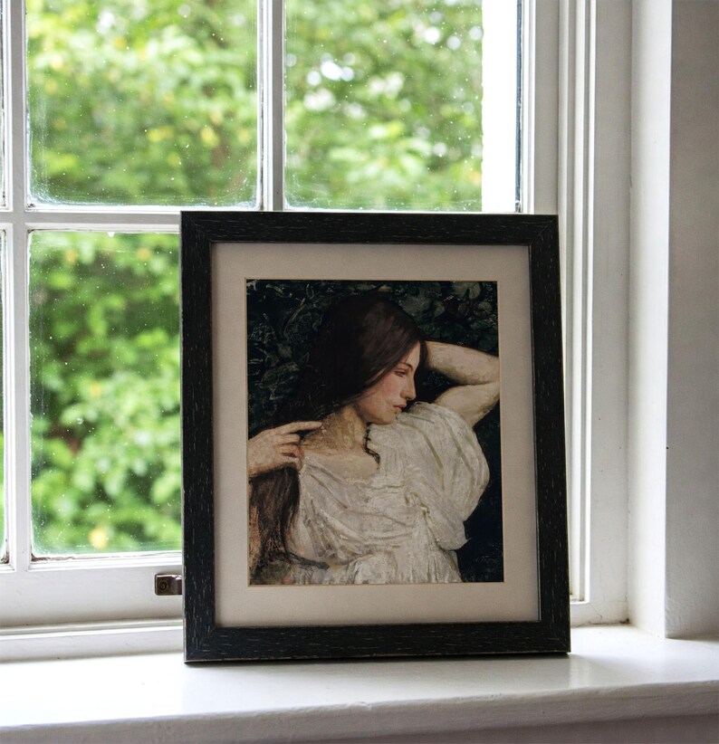 May include: A framed black and white portrait of a woman with long dark hair, wearing a white dress, looking down and resting her head on her arm.