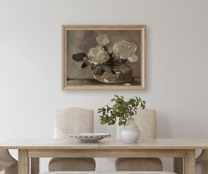 May include: A framed painting of white roses in a vase. The painting is in a light wood frame and is hanging on a white wall. The roses are in a clear glass vase with a white background. The painting is in a minimalist style.